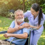 Happy nurse holding elderly man hand on wheelchair in garden at